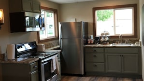 A kitchen with a stainless steel refrigerator, stove, microwave, and oven. There is a window with a view of trees and a sink with a faucet. - Glacier Basecamp Lodge (Columbia Falls)