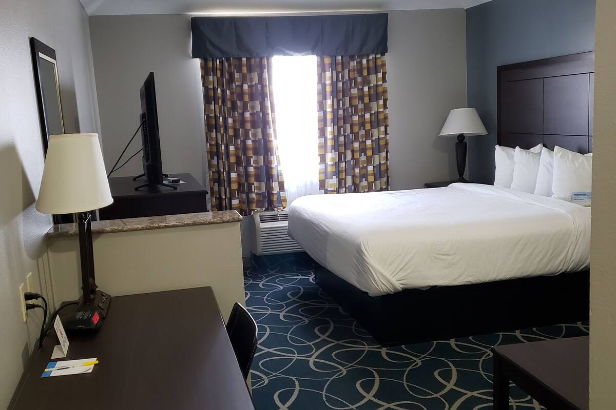 A hotel room with a bed, desk, chair, and a television.