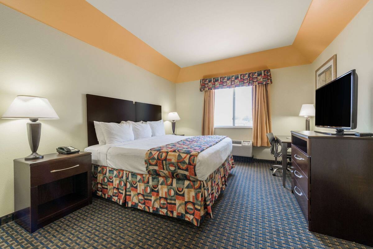 A hotel room with a bed, bedside tables, a desk, a television, and a window with curtains.