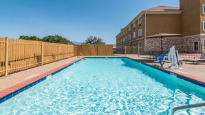 Una piscina con una recinzione in legno, una sedia per il bagnino e un edificio con molte finestre sullo sfondo.