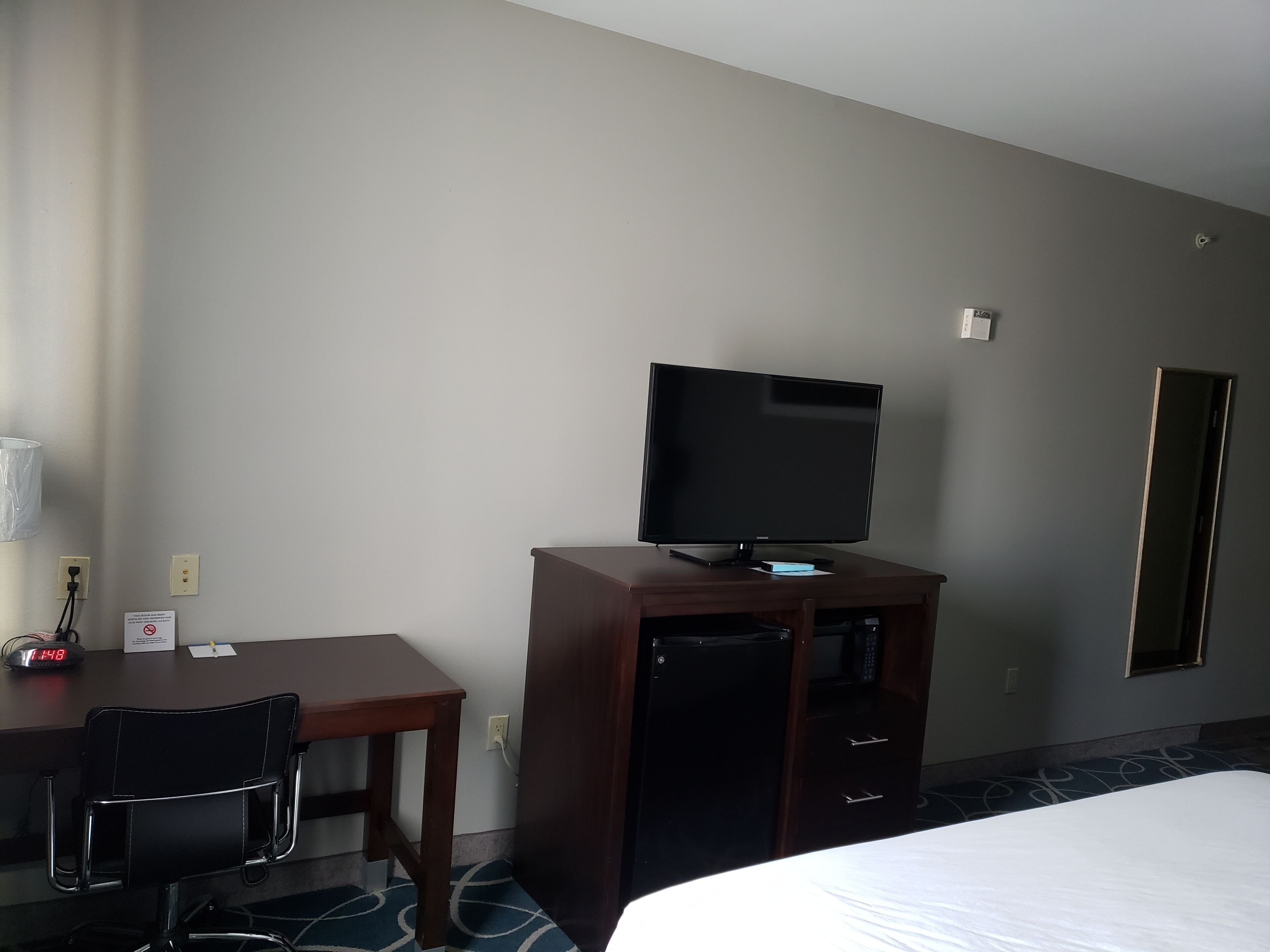 Habitación de hotel con cama, escritorio con silla, televisor sobre un soporte de madera y armario.