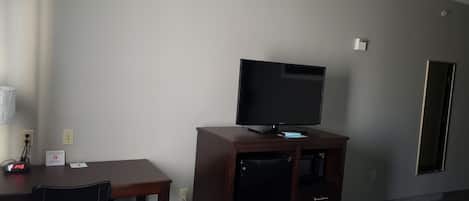 Habitación de hotel con cama, escritorio con silla, televisor sobre un soporte de madera y armario.