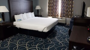 Una camera d'albergo con un letto grande, due comodini con lampade, una scrivania con una sedia, una finestra con tende a motivi e un condizionatore d'aria a parete.