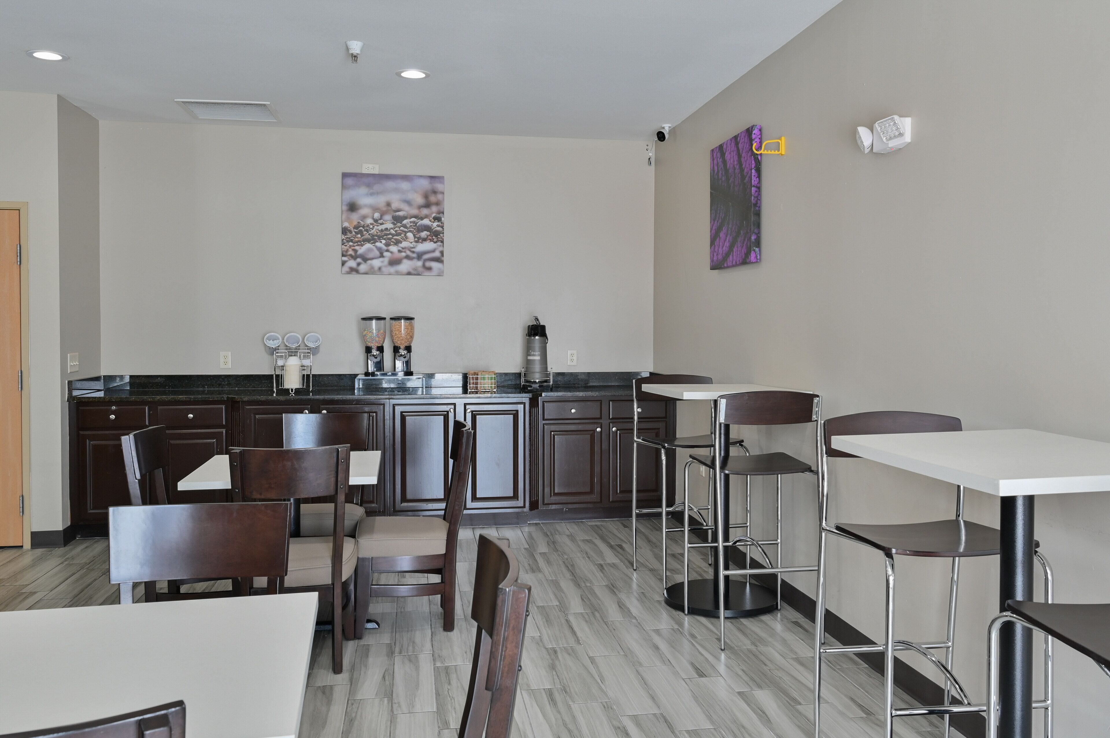 Una cocina moderna con armarios de madera oscura, encimera de mármol y una estación de café. Hay taburetes de bar y una mesa de comedor con sillas.