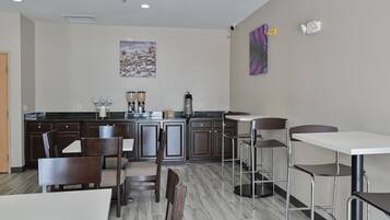 Una cocina moderna con armarios de madera oscura, encimera de mármol y una estación de café. Hay taburetes de bar y una mesa de comedor con sillas.