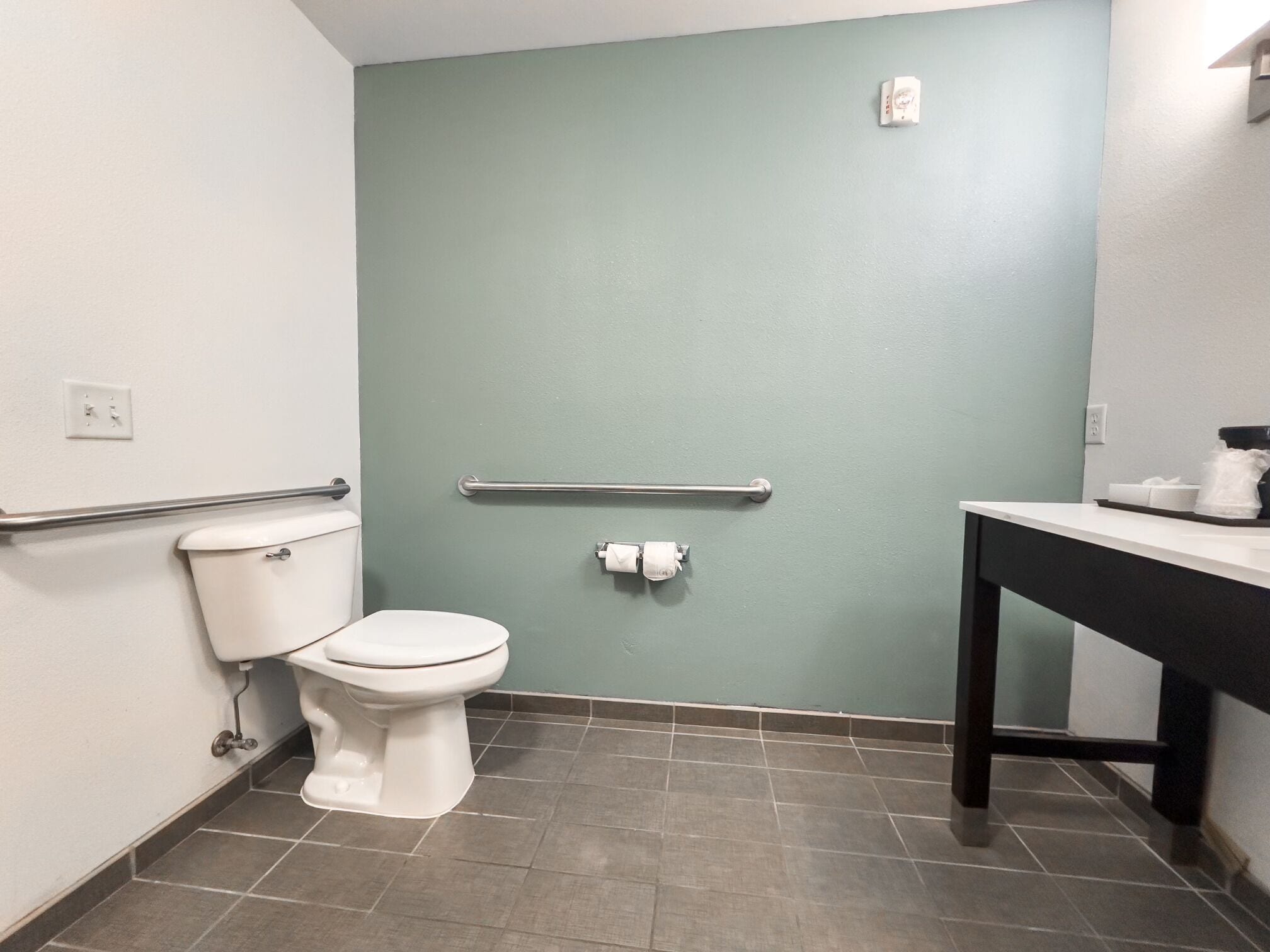 A small bathroom with a toilet, a handrail, and a sink.