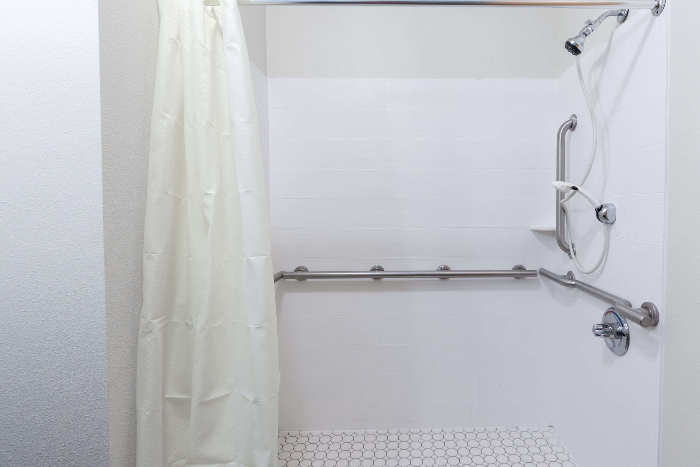 A shower area with a grab bar, a showerhead, and a curtain.