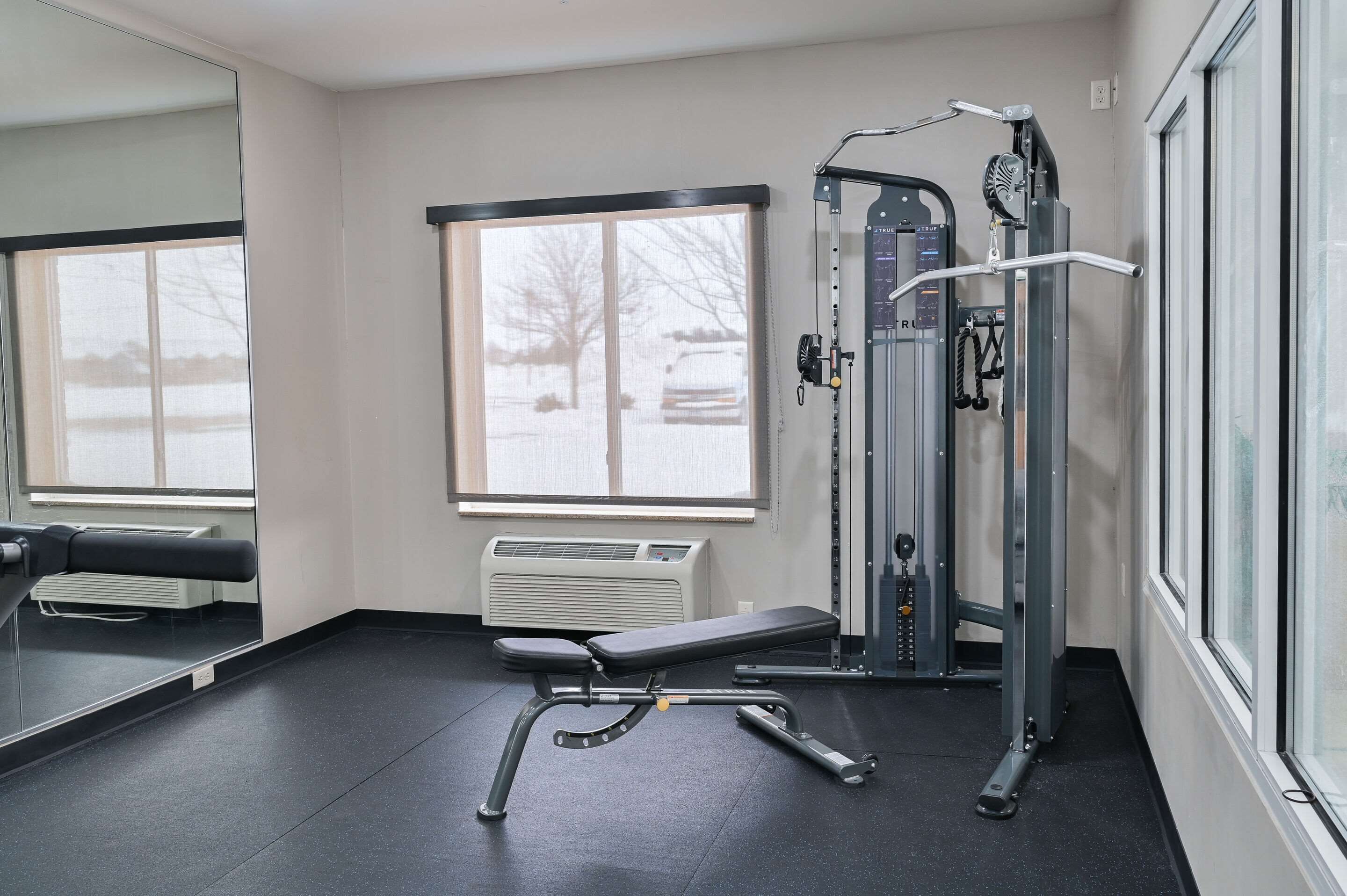 Un gimnasio con una banca, máquinas de pesas y un ventanal grande.