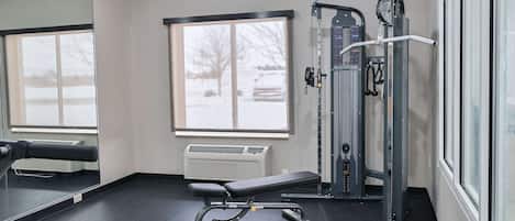 Un gimnasio con una banca, máquinas de pesas y un ventanal grande.