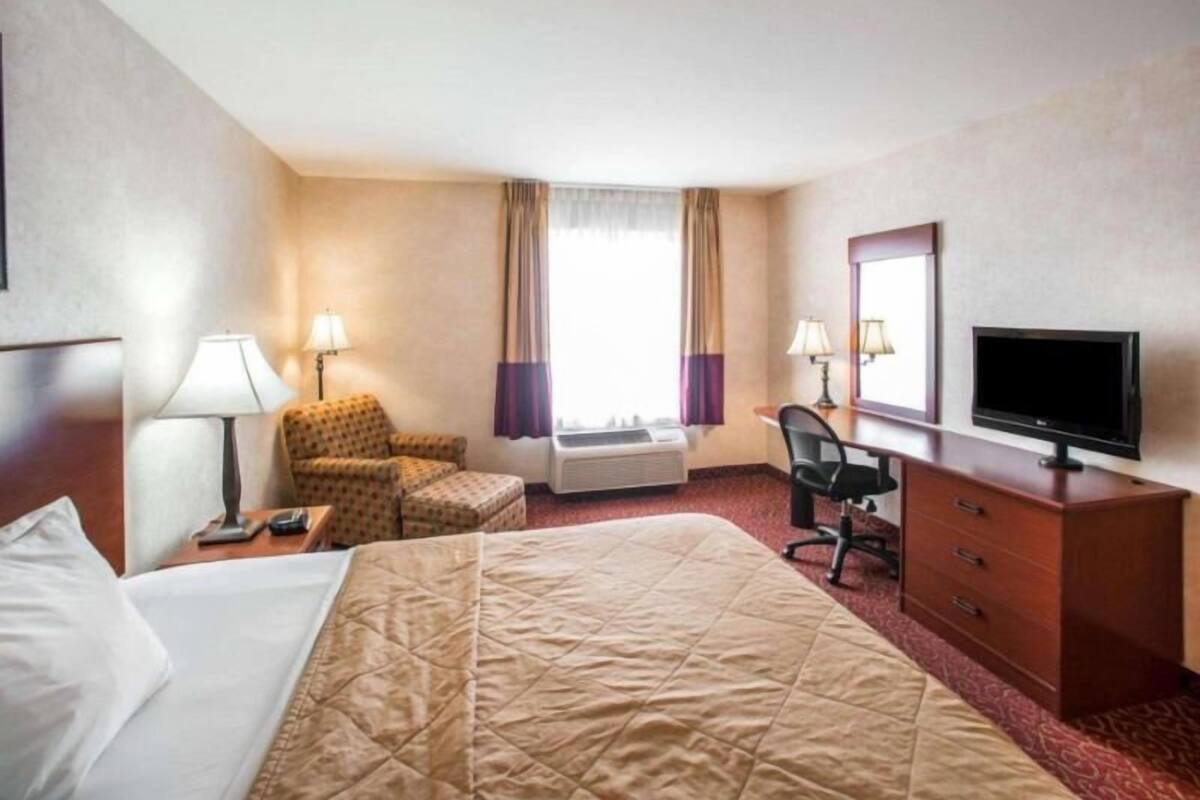 A hotel room with a bed, a desk, a chair, a television, and a window with curtains.