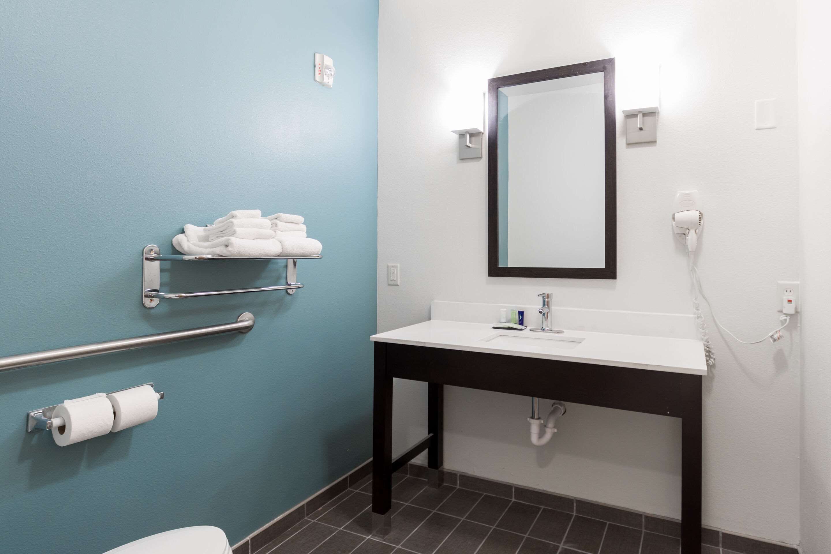 Un baño con pared azul, un lavamanos blanco, un espejo, un toallero y un porta papel higiénico.