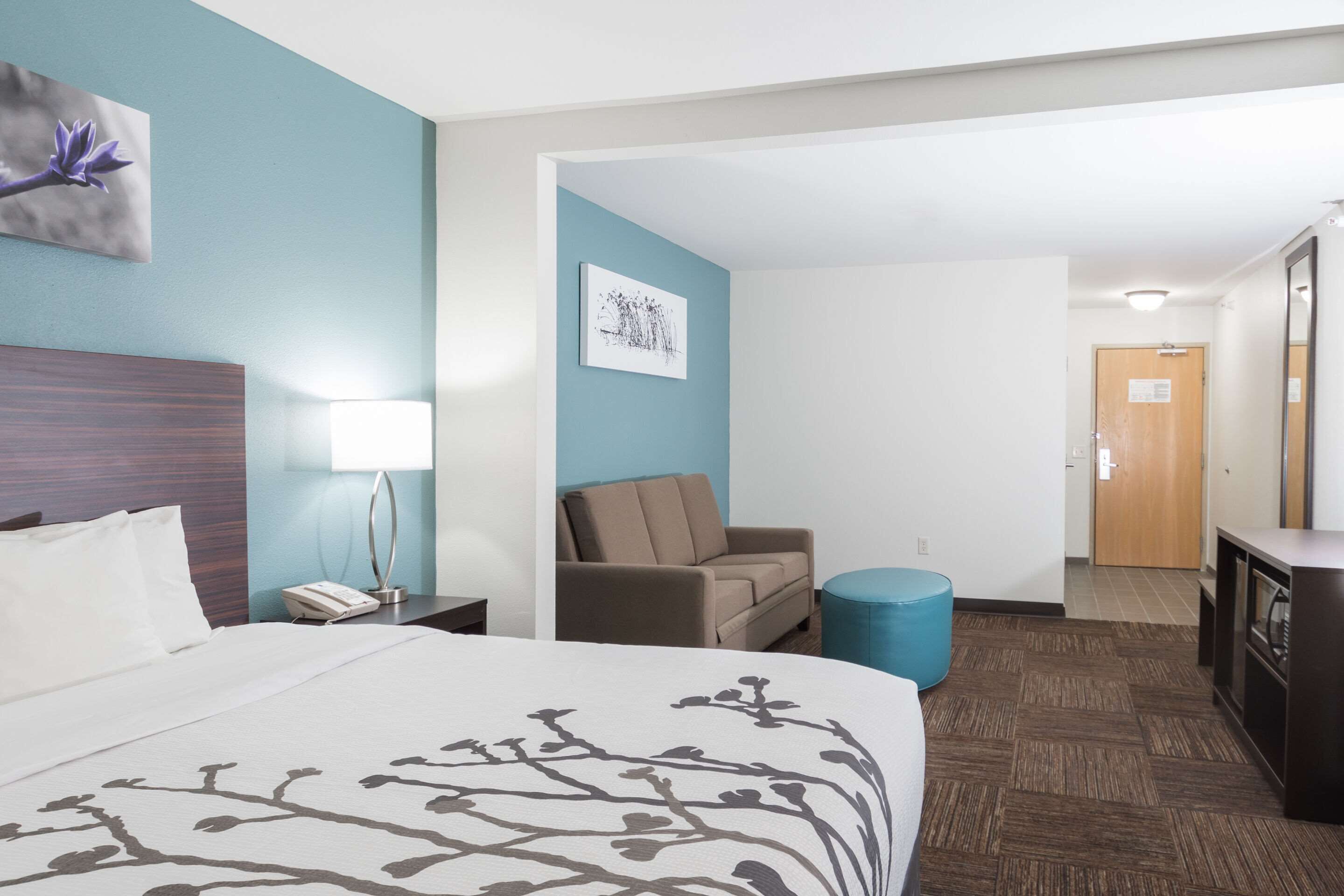 Quarto de hotel com cama, escrivaninha, poltrona, sofá, luminária e um quadro na parede.