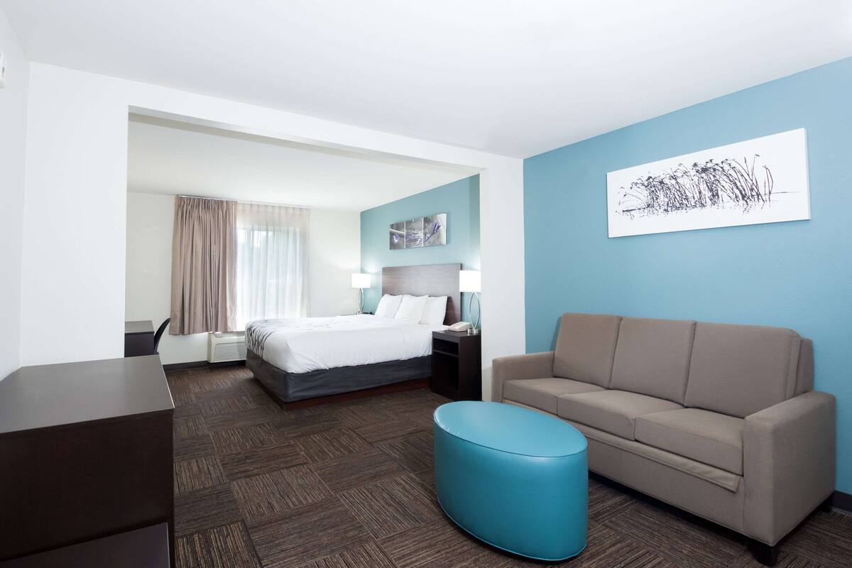 A hotel room with a bed, a sofa, a desk, and a blue ottoman.