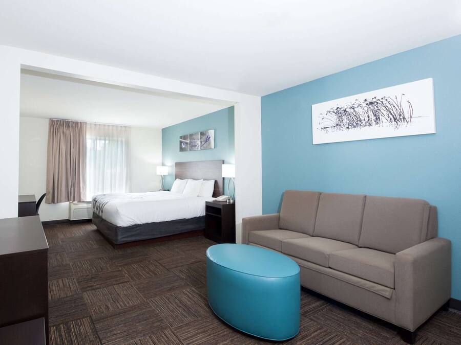 A hotel room with a bed, a sofa, a desk, and a blue ottoman.