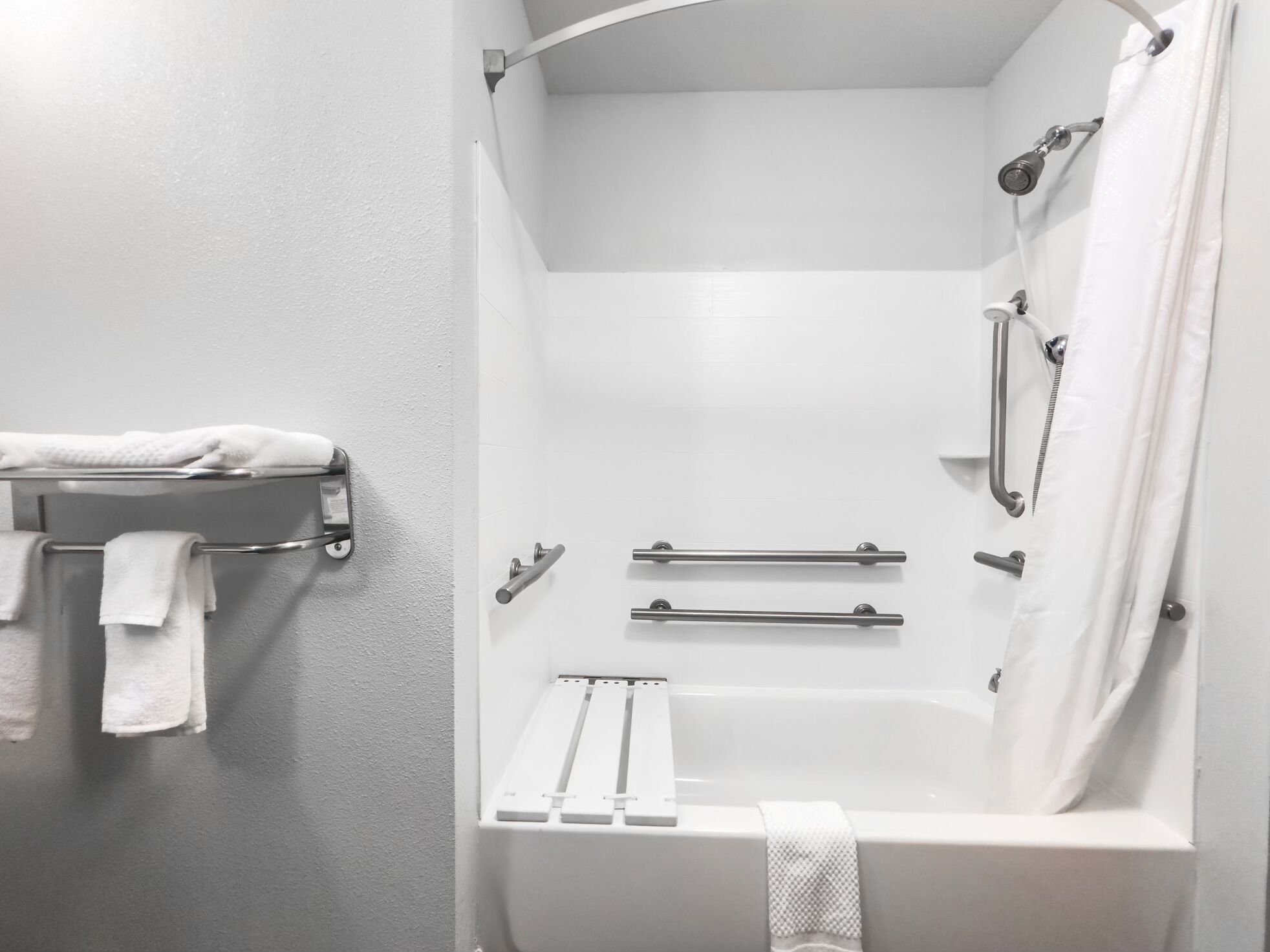 A modern bathroom with a bathtub, shower, and handrails.
