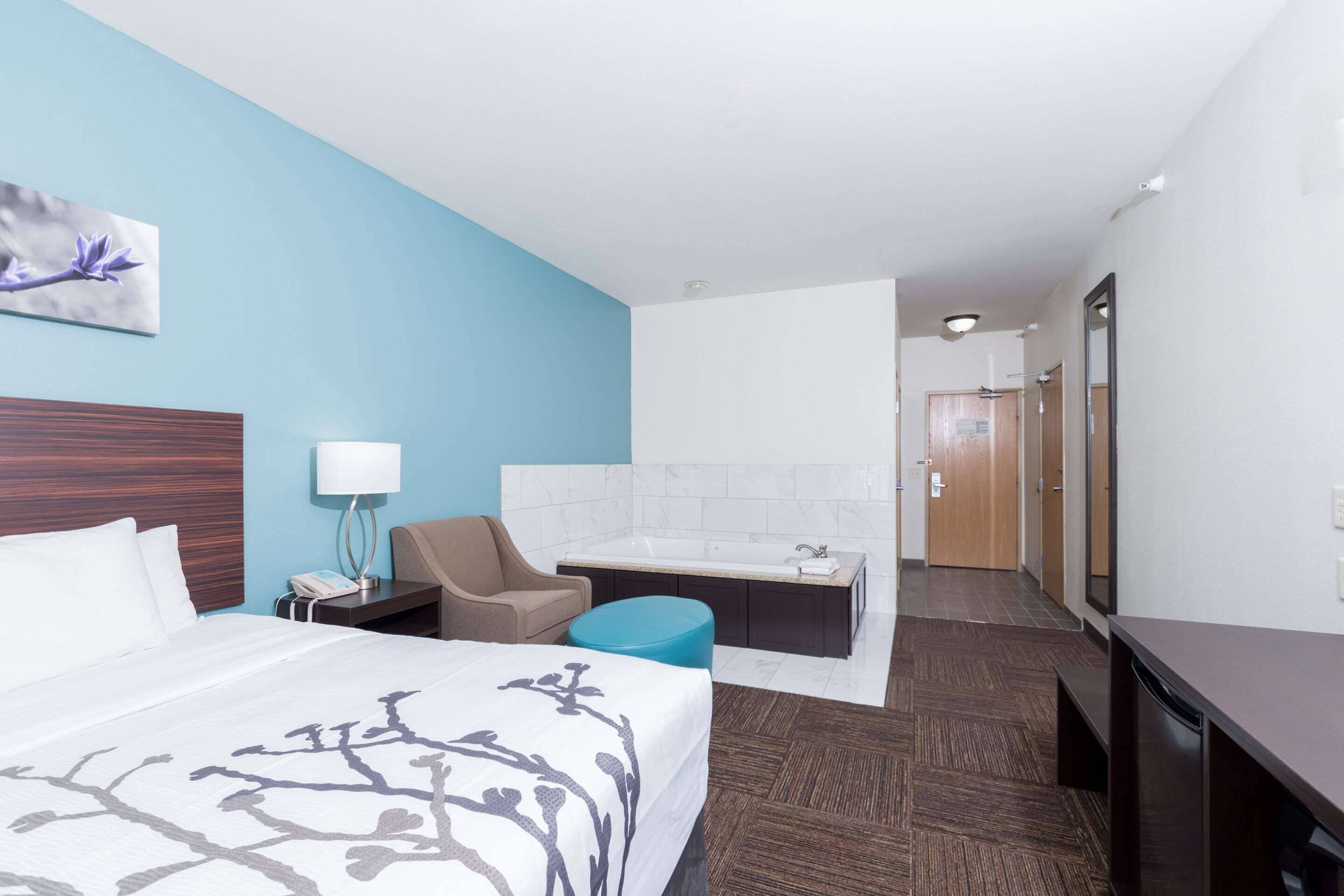 Une chambre d’hôtel avec un grand lit, un bureau, une chaise, une salle de bain avec baignoire et un miroir.