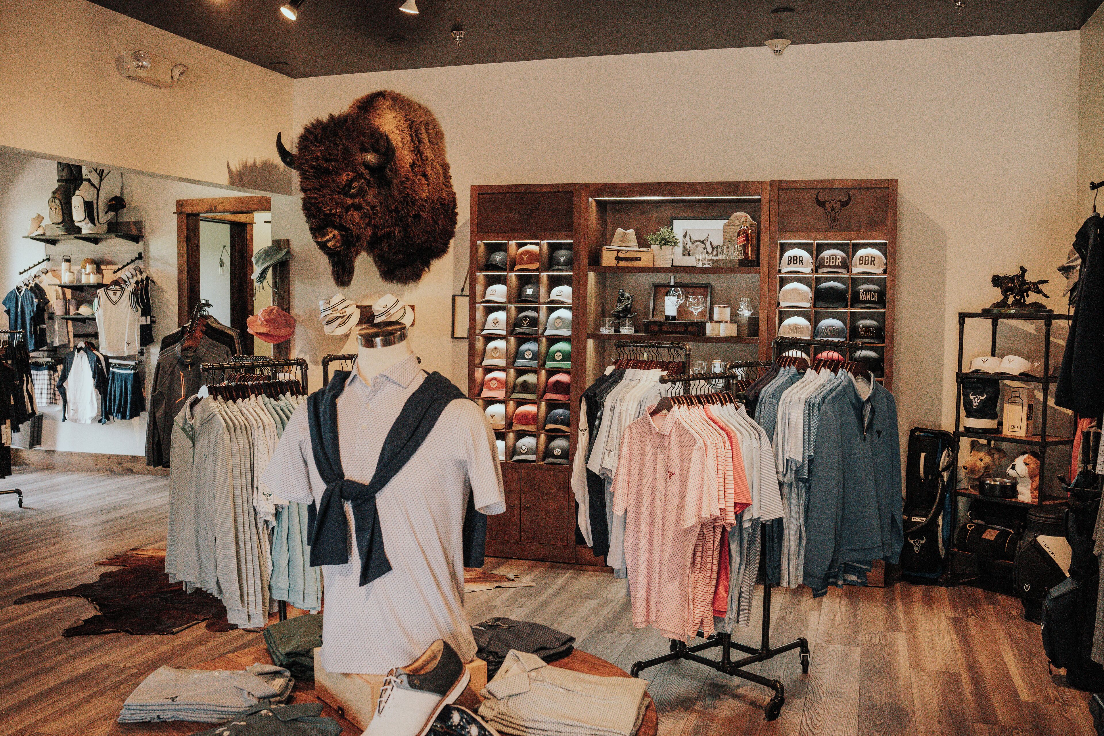 A clothing store with racks of clothes, a mannequin, and a display of hats.
