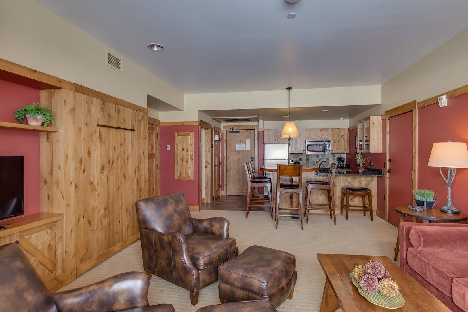 A living room with a fireplace, a television, leather armchairs, a sofa, a dining area with a table and chairs, and a kitchen with a microwave.
