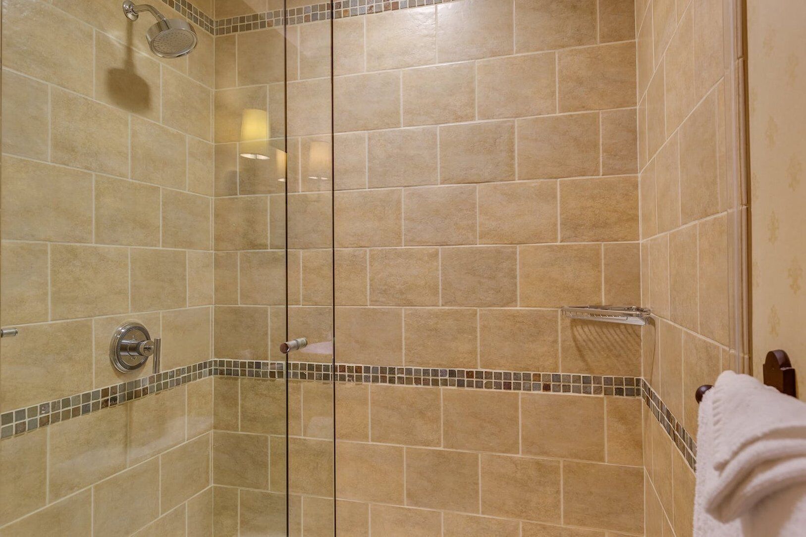 A shower with beige tiles and a glass door, a towel rack, and a showerhead.