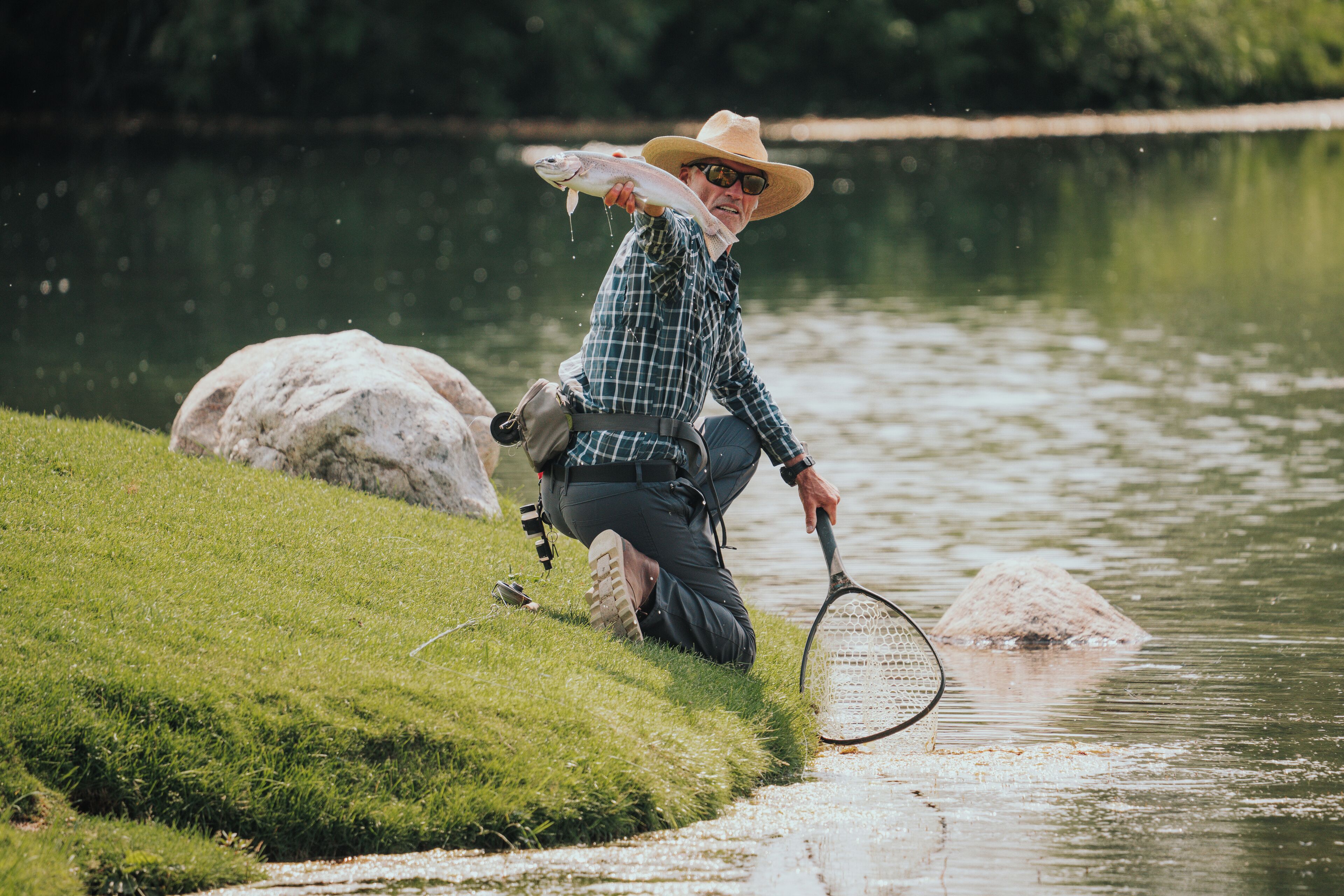 A person holding a fish near a body of water with rocks and grass.