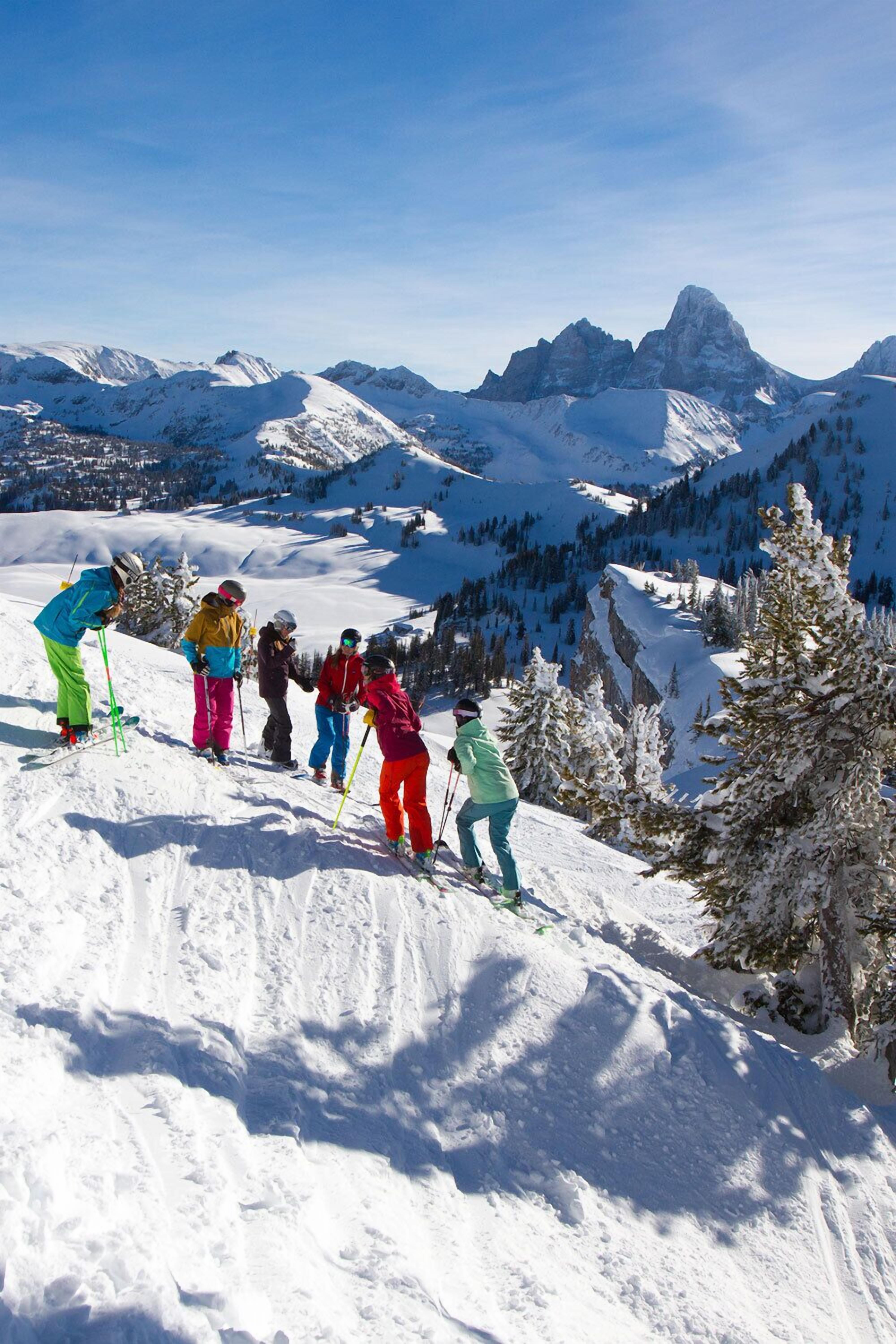A group of skiers on a snowy mountain slope with a clear view of the surrounding peaks.