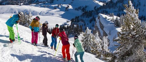 A group of skiers on a snowy mountain slope with a clear view of the surrounding peaks.