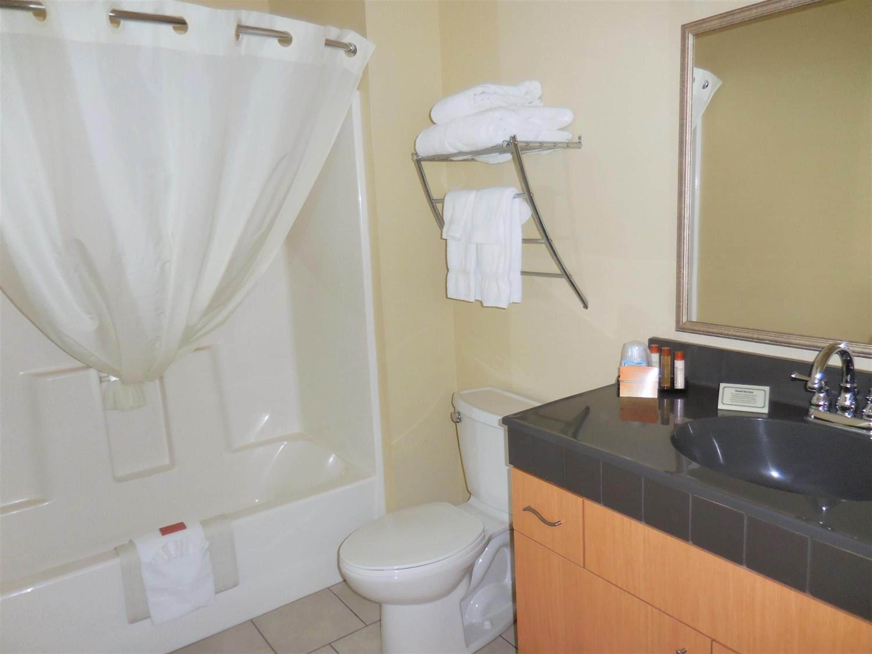Un baño con bañera, inodoro y tocador con lavamanos y espejo.