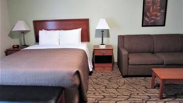 Een hotelkamer met een groot bed, twee nachtkastjes, een bruine bank, een klein tafeltje en een kamerbreed tapijt met een patroon.