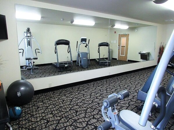 Un gimnasio con equipo de ejercicio, un espejo grande y suelo alfombrado.