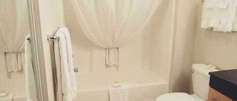 A bathroom with a bathtub, toilet, and a glass shower enclosure.