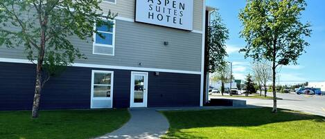 The Aspen Suites Hotel building with a sign, a paved driveway, and a grassy area with trees.