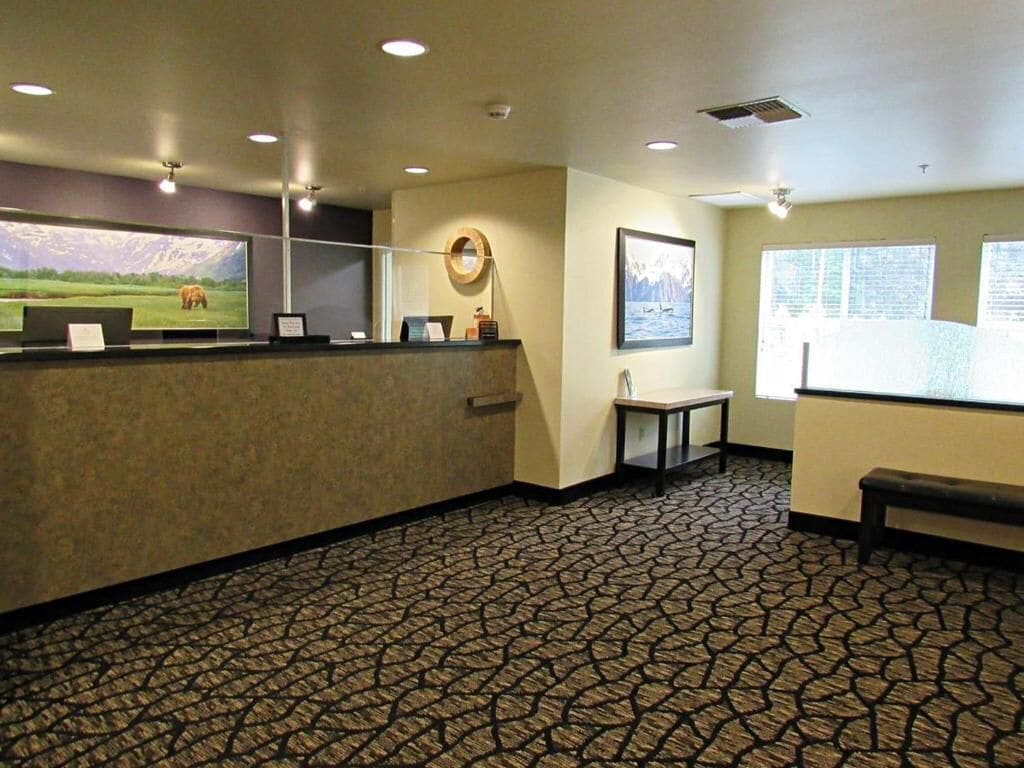 A reception area with a reception desk, a wall-mounted screen, a round mirror, and a framed picture.