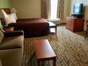 A hotel room with a bed, a sofa, a small table, a TV on a cabinet, and patterned carpet.