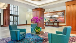 Un hall d’entrée avec des fauteuils turquoise, une moquette à motifs, un comptoir d’accueil et une grande fenêtre.