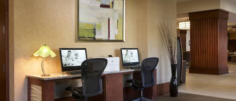 A hotel workspace with two desks, computers, chairs, a lamp, and a decorative wall piece.