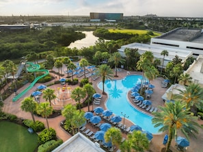 Un complexe hôtelier doté d’une piscine, de chaises longues, de palmiers et d’un toboggan aquatique.
