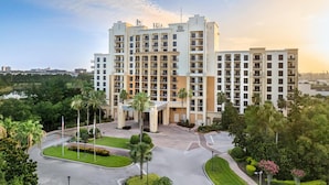 Un hôtel à plusieurs étages, doté d’une entrée principale et entouré de verdure, avec un espace de stationnement à proximité.