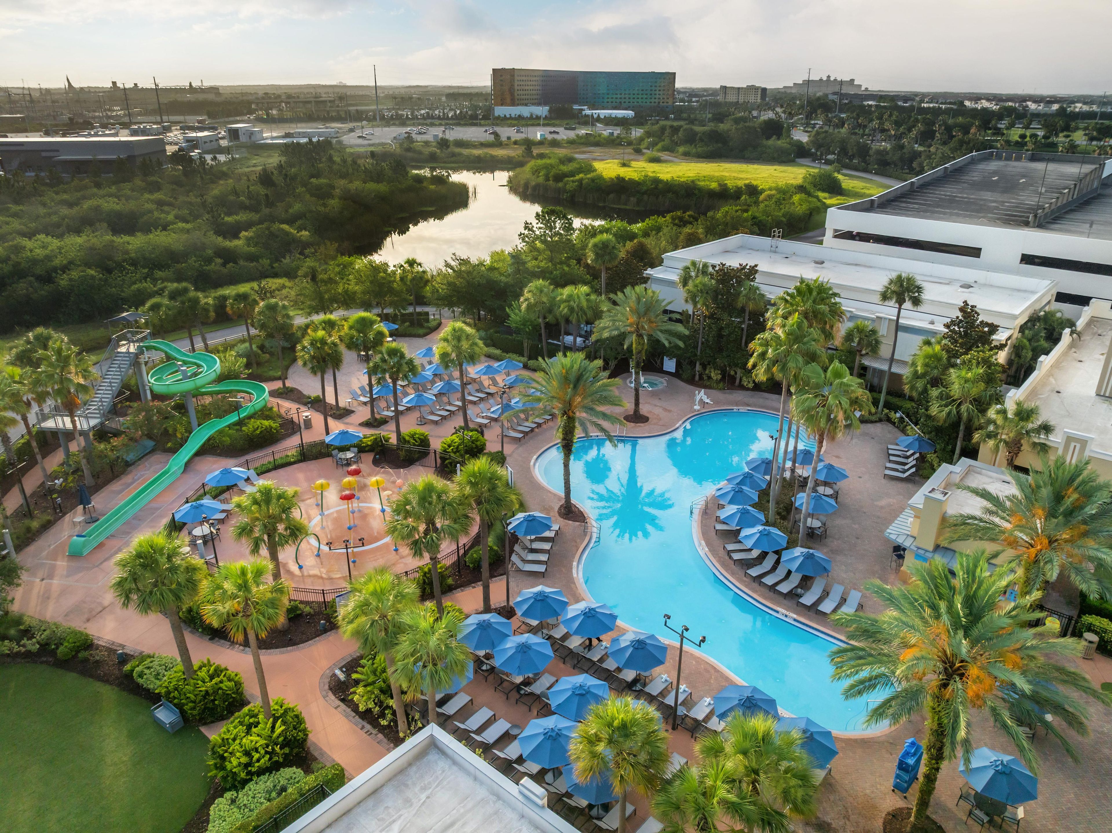 A resort with a swimming pool, lounge chairs, palm trees, and a water slide.