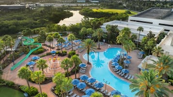 A resort with a swimming pool, lounge chairs, palm trees, and a water slide.