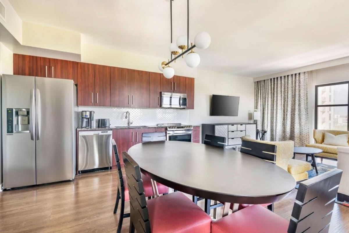 Een moderne keuken met roestvrijstalen apparatuur, een eetgedeelte met een ronde tafel en stoelen, en een zithoek met een bank en televisie.