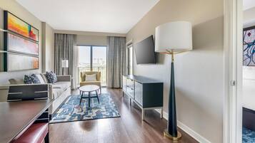 A modern hotel room with a sofa, a dining table, a TV, and a floor lamp.