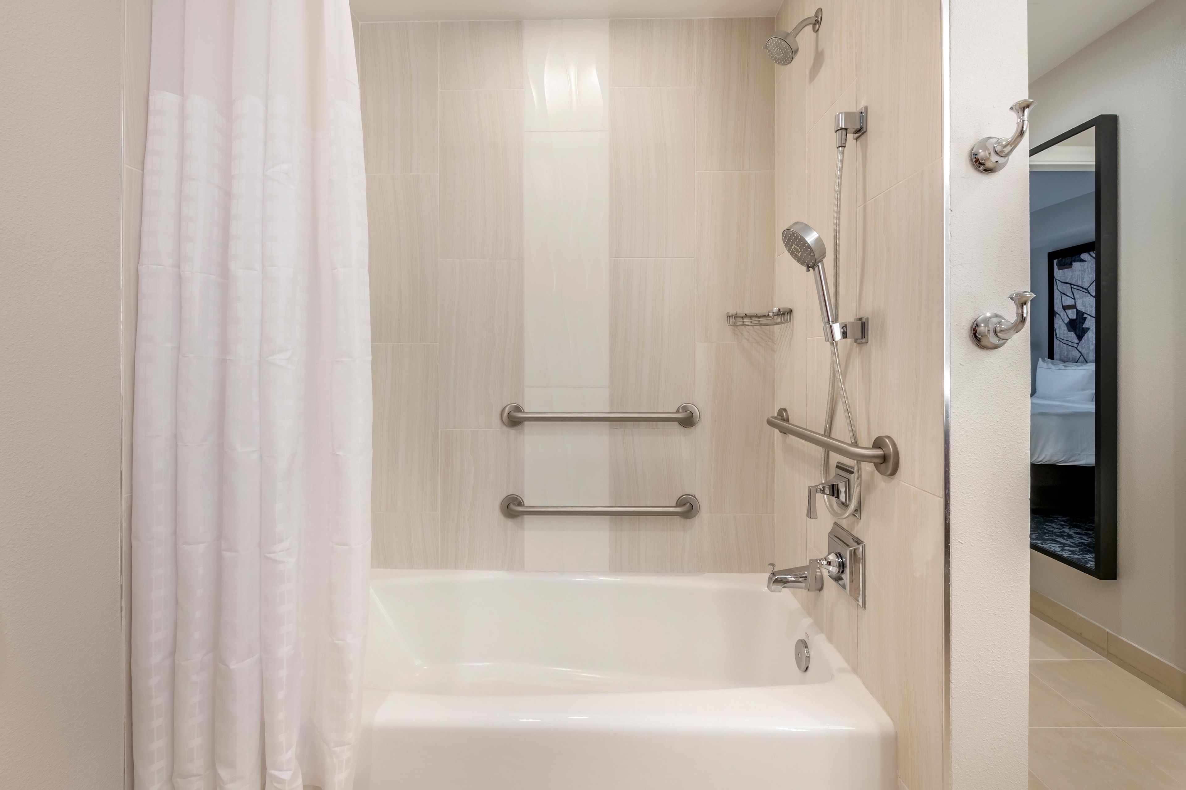 A modern bathroom with a bathtub, shower, and handrails.