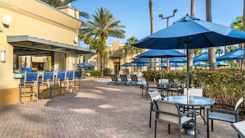 An outdoor patio area with seating and umbrellas, a pool, and a building with a sign for an 'Exercise Center.'