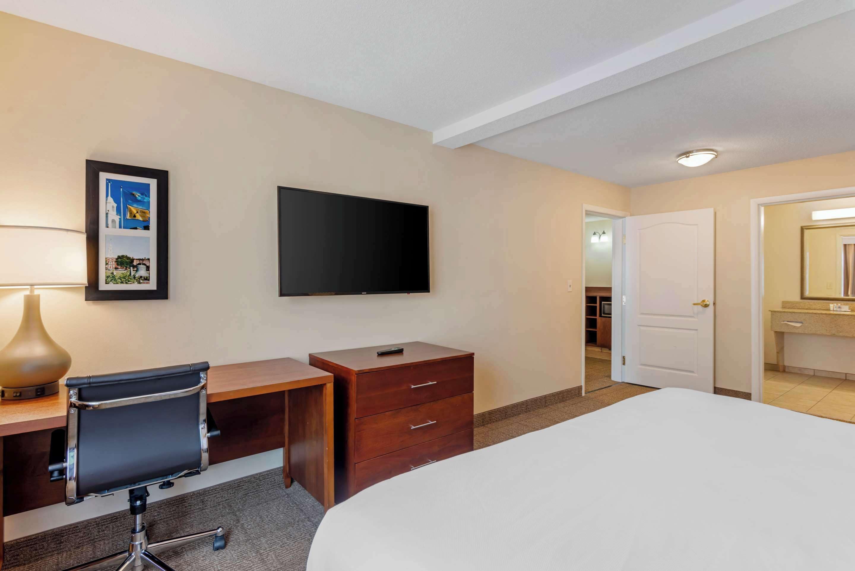 A hotel room with a bed, desk, chair, TV, and a framed picture on the wall.
