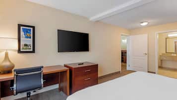 Habitación de hotel con cama, escritorio, silla, televisor y un cuadro en la pared.