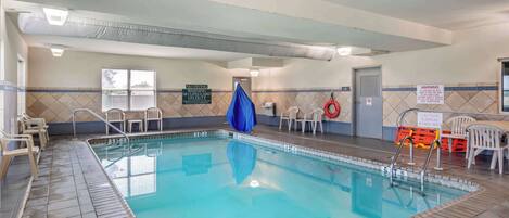 An indoor swimming pool with clear water, marked depth lines, and safety signs.
