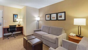 A hotel room with a sofa, a desk with a chair, a lamp, and framed pictures on the wall.