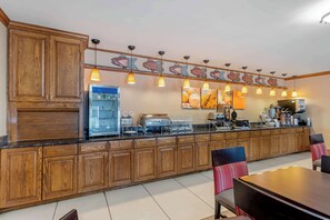A kitchen with wooden cabinets, a refrigerator, a coffee machine, and a dining area with chairs and a table.