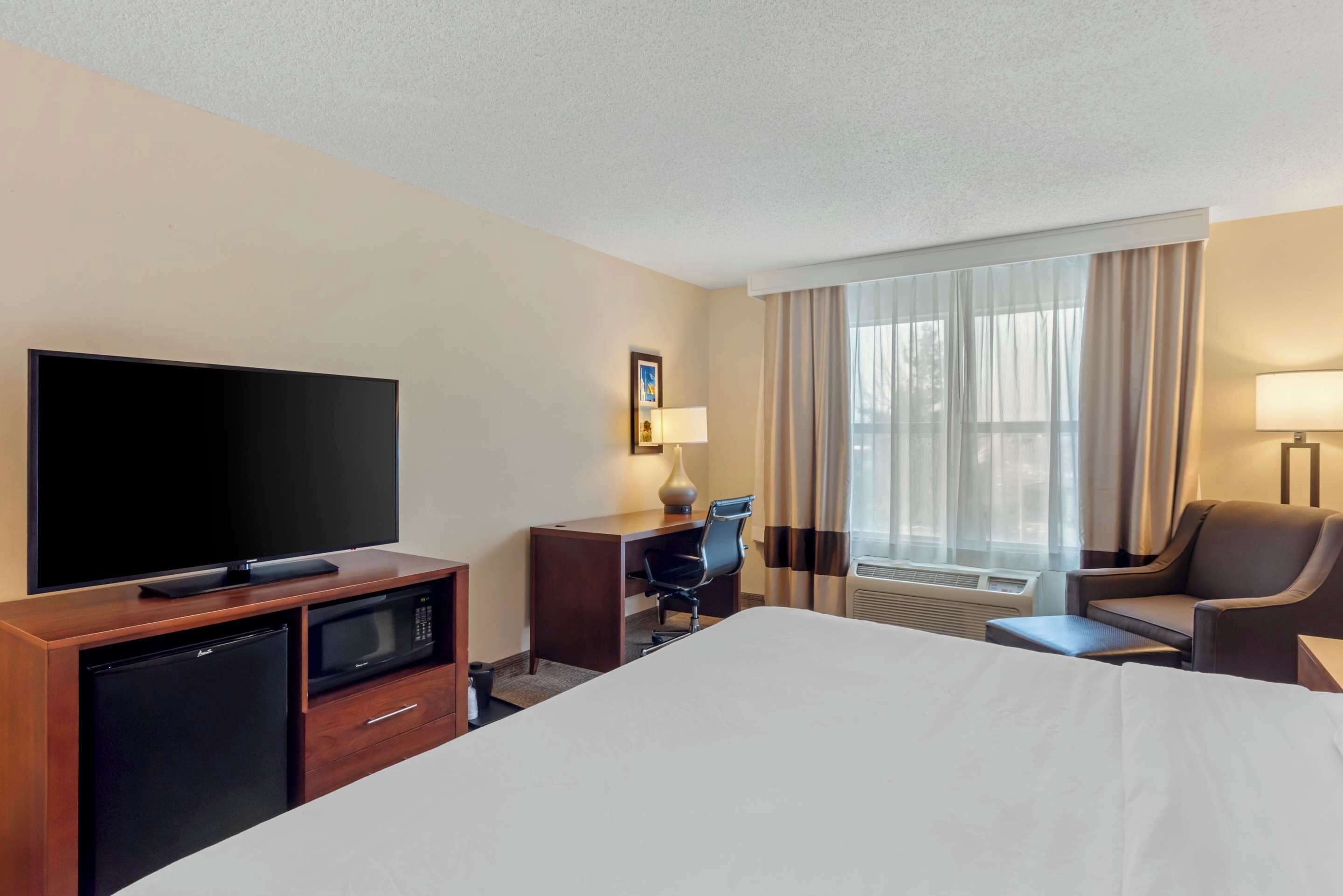 A hotel room with a large bed, a flat-screen TV, a desk with a chair, a microwave, a refrigerator, and a window with curtains.
