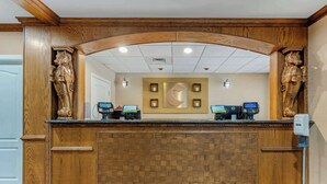 A reception desk with two computer monitors, a wooden reception area, and a large wall clock.